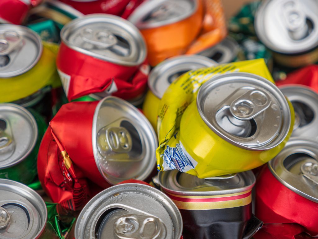 A pile of crushed and colorful aluminum drink cans, including red, yellow, and orange cans, closely stacked together.