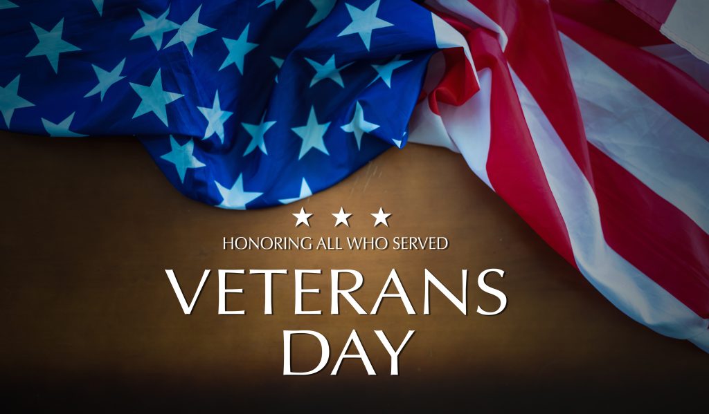 A folded American flag on a dark background with text that reads: "Honoring All Who Served. Veterans Day." Three white stars are above the text.